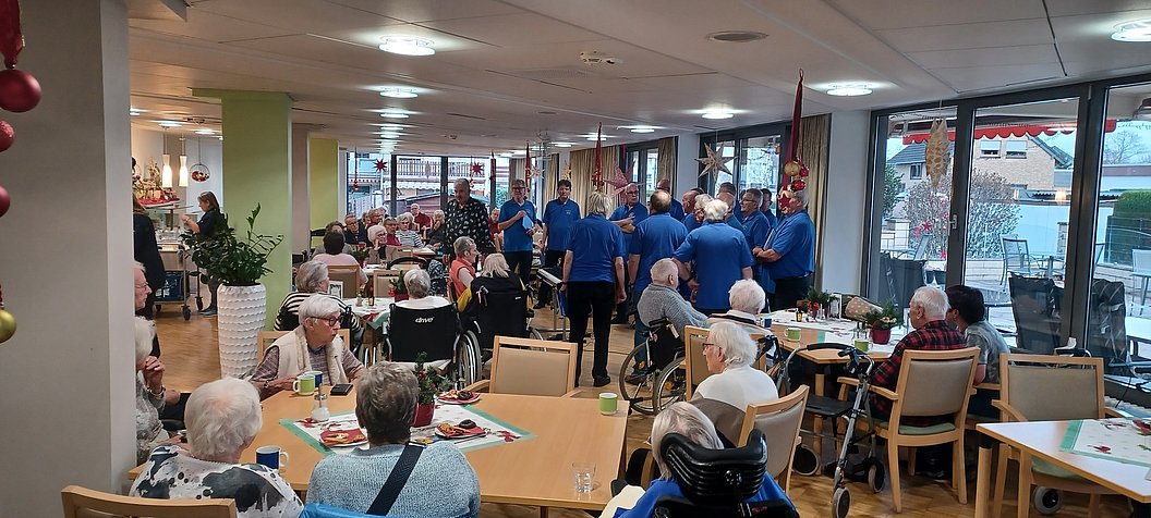 Gemütliche Atmosphäre in einem Gemeinschaftsraum mit Gästen und einem Männerchor in blauen Shirts.