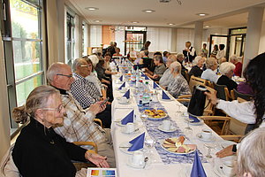Gesellige Runde von Senioren bei einer Feier mit Tischen, Teetassen und Snacks