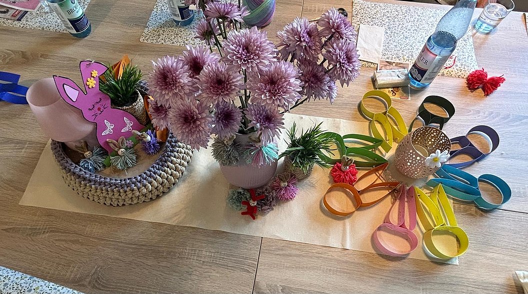 Tischdekoration mit rosa Blumen in Vasen, bunten Papierblumen und einem Hasen aus Papier auf einem hellen Läufer