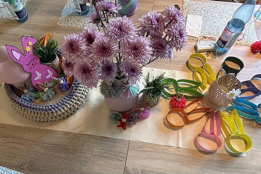 Tischdekoration mit rosa Blumen in Vasen, bunten Papierblumen und einem Hasen aus Papier auf einem hellen Läufer