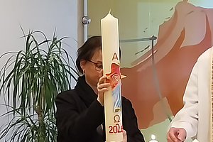 Person hält eine große weiße Kerze mit der roten Jahreszahl '2024' und dem Omega-Symbol