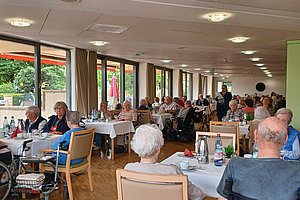 Belebte Restaurantansicht mit älteren Gästen an Tischen, helles Ambiente mit großen Fenstern.