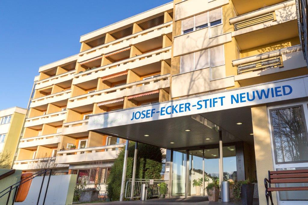 Mehrstöckiges Gebäude mit Eingangsüberdachung, auf der 'JOSEF-ECKER-STIFT NEUWIED' steht.
