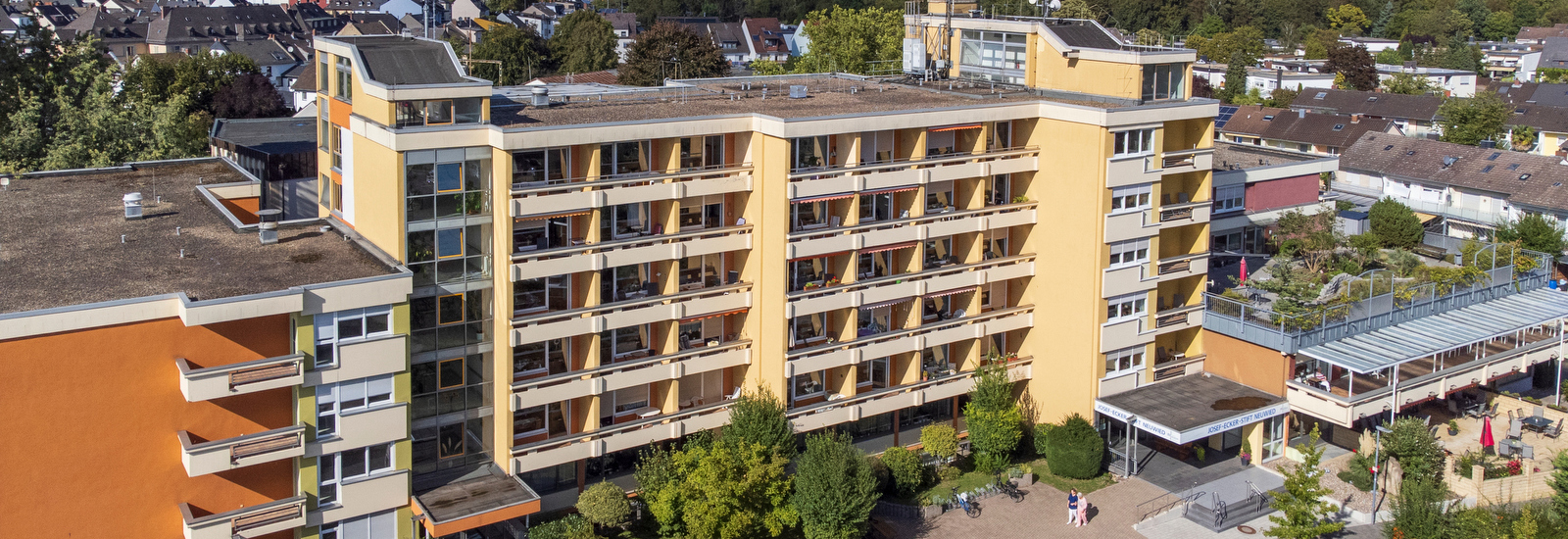 Mehrstöckiges Wohngebäude mit Balkonen, umgeben von Bäumen und weiteren Häusern in einer Wohngegend.