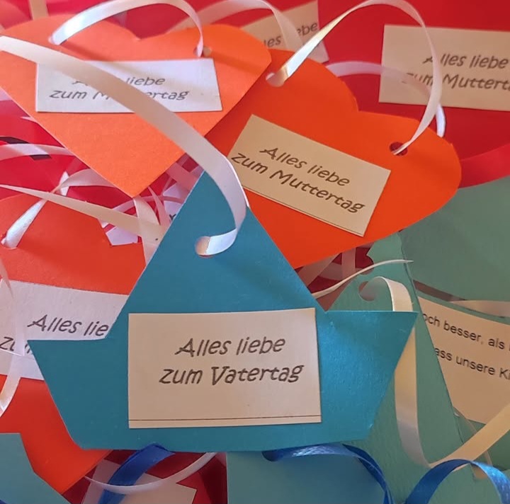 Bunte Geschenkanhänger in Form von Booten, mit Sprüchen zum Mutter- und Vatertag.